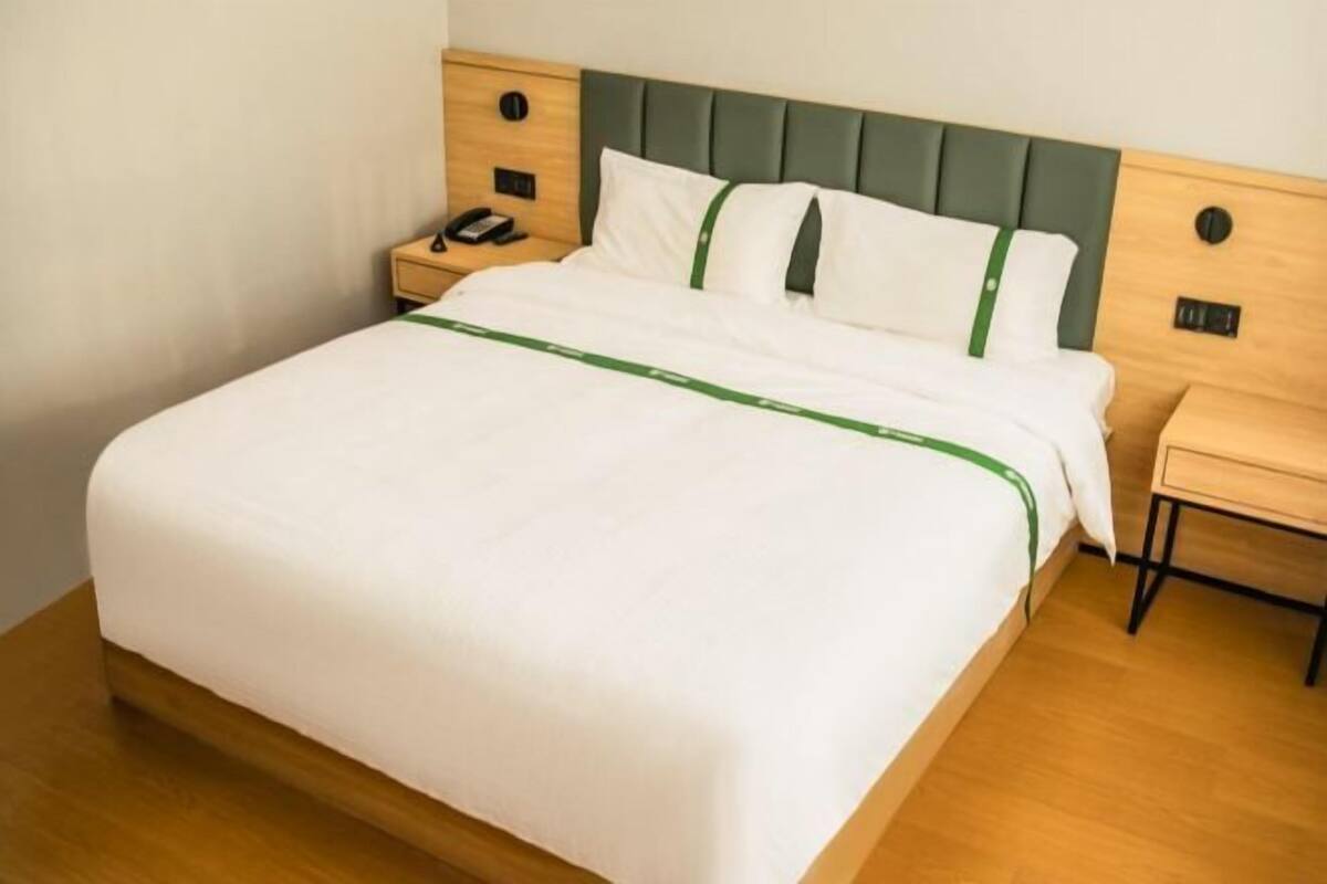 A neatly made bed with a green accent, a bedside table with a phone, and a wooden nightstand.