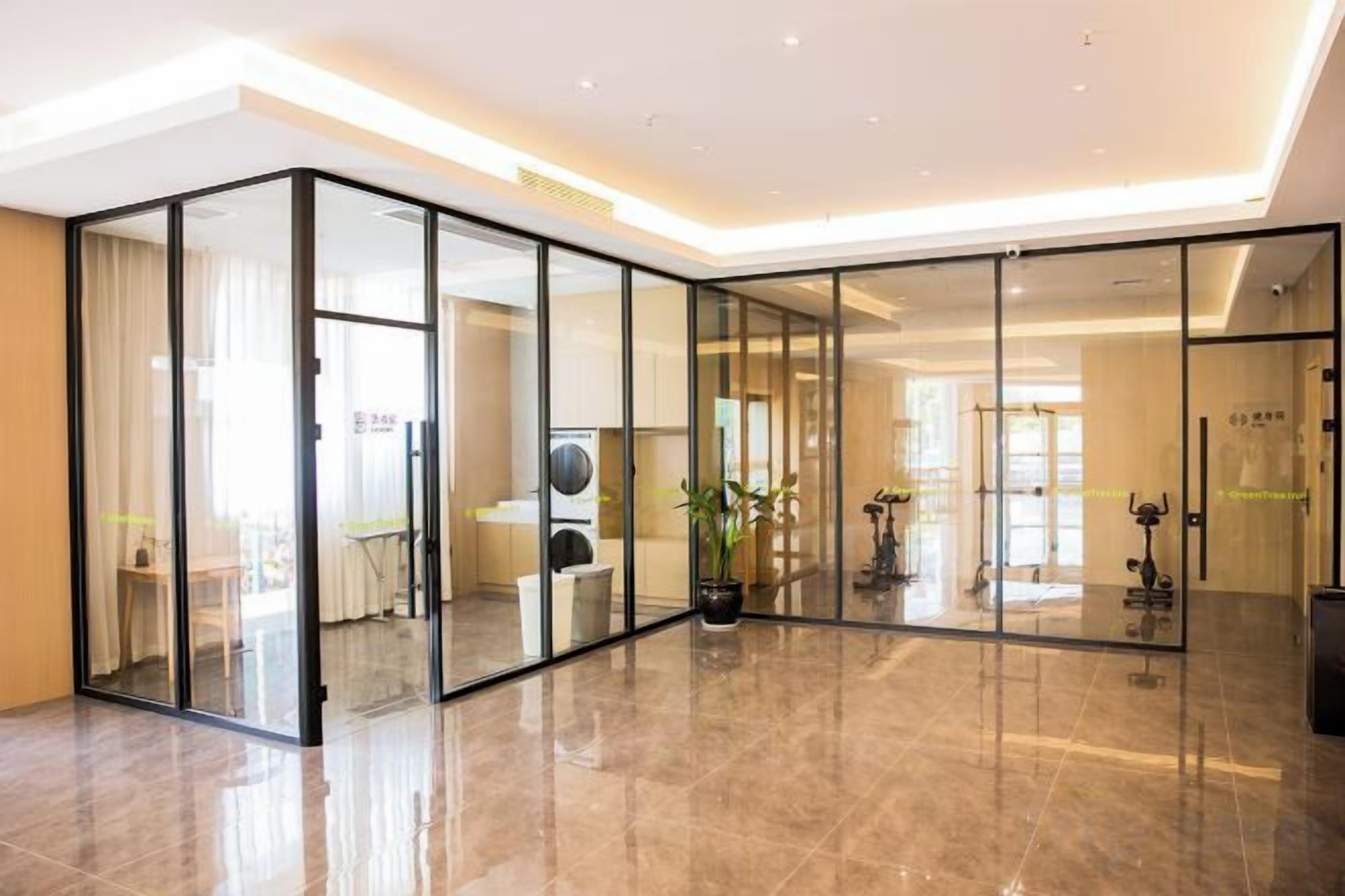 A modern hotel lobby with a glass partition, a large potted plant, and a visible exercise machine.
