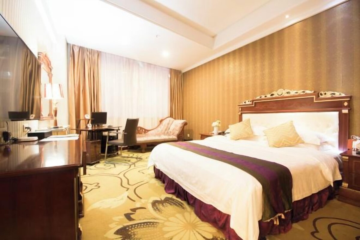 Ein Hotelzimmer mit einem großen Bett, einem Schreibtisch, einem Sessel und einem Fernseher.