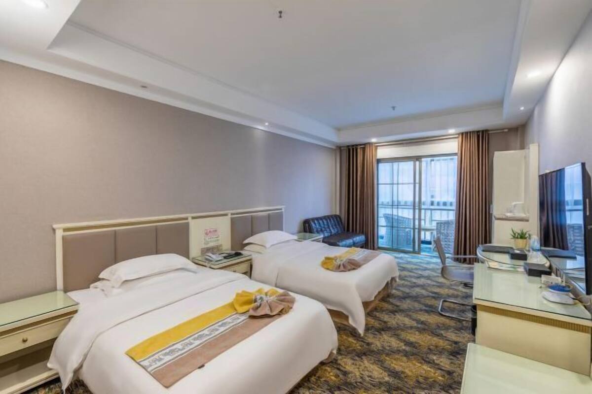 Ein Hotelzimmer mit zwei Betten, einem Schreibtisch, einem Stuhl, einem Balkon mit Blick und einem großen Fenster.