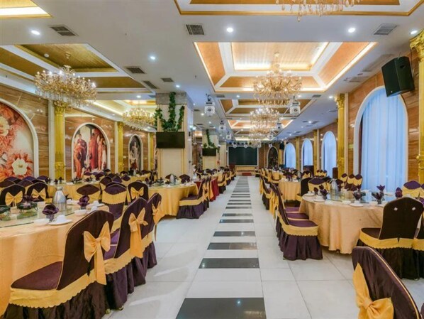 Une salle de banquet avec des rangées de tables et de chaises, des lustres et des fresques murales.