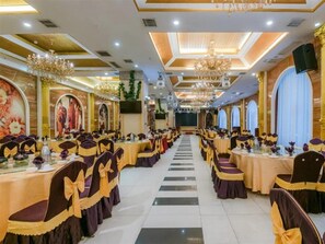 Une salle de banquet avec des rangées de tables et de chaises, des lustres et des fresques murales.