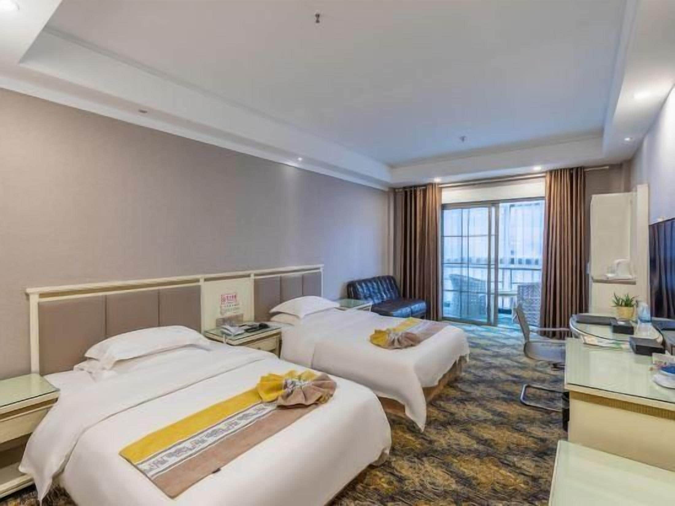 Habitación de hotel con dos camas, un escritorio, una silla y un ventanal grande.