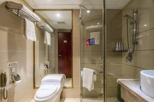 Un baño de hotel con ducha de vidrio, un lavamanos con espejo y un inodoro.
