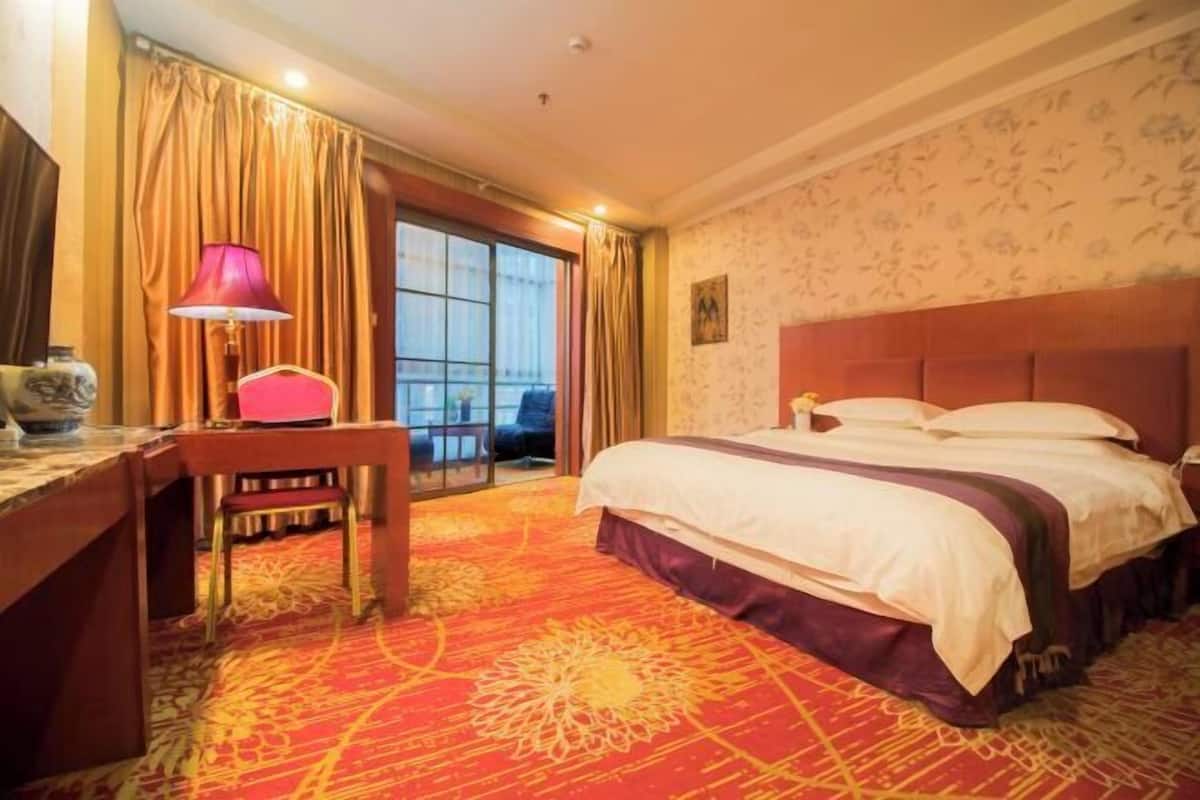 Ein Hotelzimmer mit einem großen Bett, einem Schreibtisch, einem Sessel und Blick ins Freie.