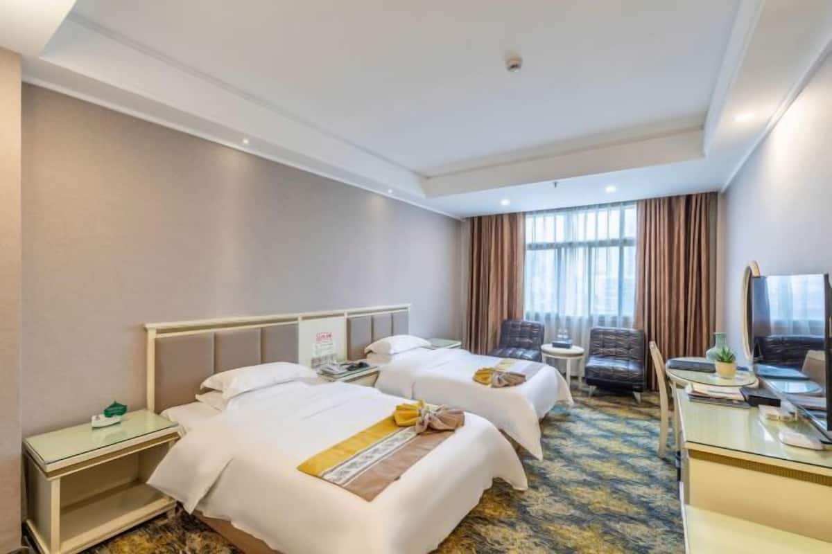Ein Hotelzimmer mit zwei Betten, einem Schreibtisch, einem Stuhl, einem Fernseher und einem Fenster mit Vorhängen.