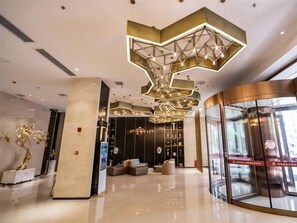 Un hall d’entrée moderne avec un luminaire au plafond aux formes géométriques, un comptoir d’accueil et un ascenseur en verre.