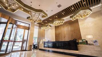 A modern hotel lobby with a reception desk, geometric ceiling lights, and large windows.