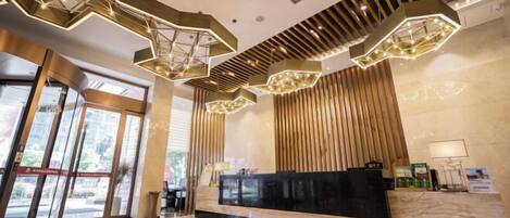Un vestíbulo de hotel moderno con una recepción, lámparas de techo geométricas y amplios ventanales.
