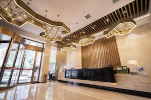 Un vestíbulo de hotel moderno con una recepción, lámparas de techo geométricas y amplios ventanales.