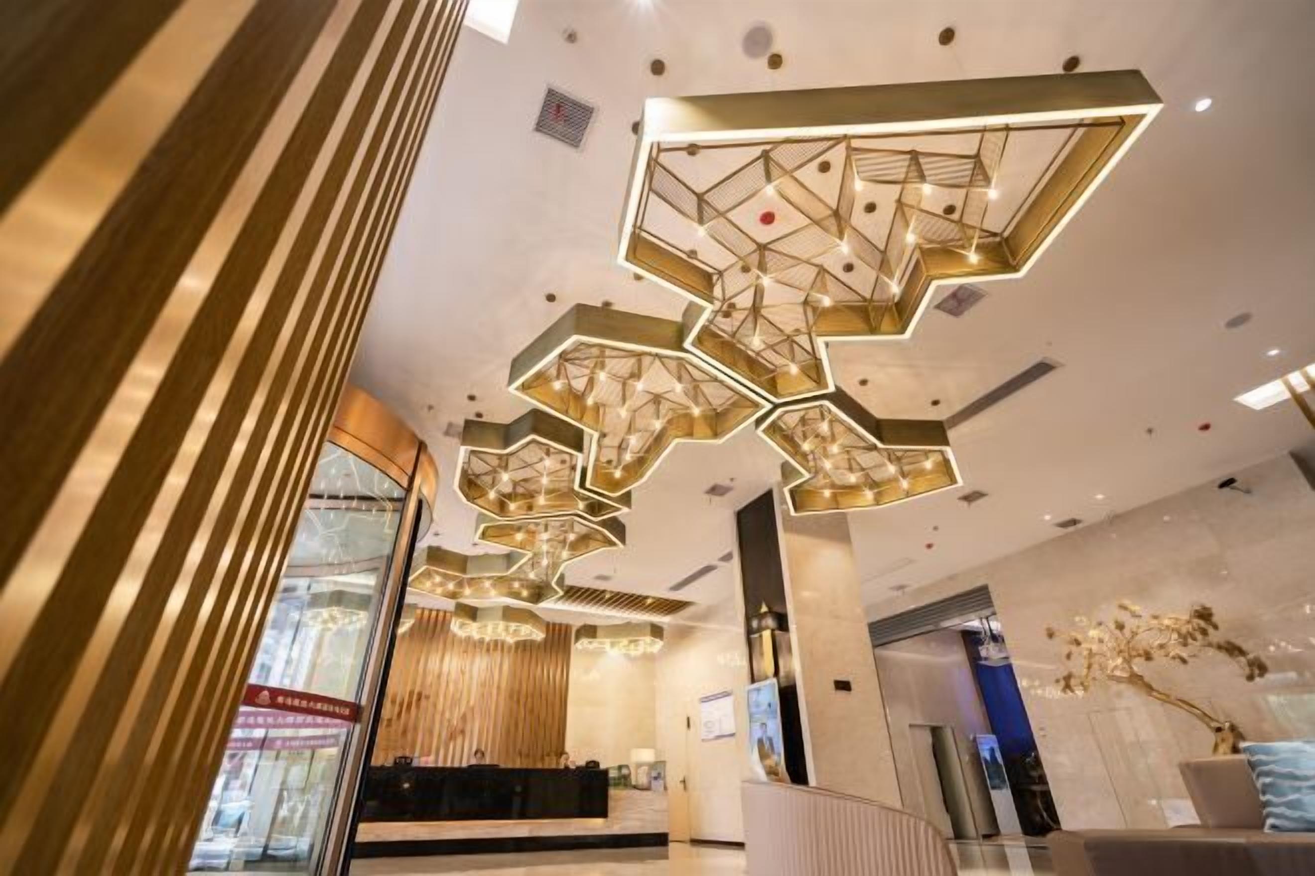A modern hotel lobby with a geometric ceiling design, a reception desk, and a large window.