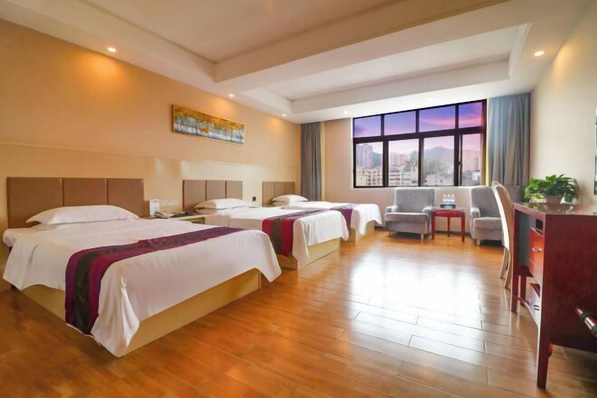 Ein Hotelzimmer mit zwei Betten, einem Schreibtisch, einem Stuhl und einem großen Fenster mit Blick auf die Stadt.