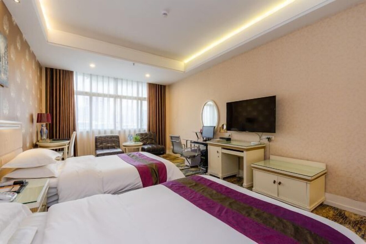 Ein Hotelzimmer mit zwei Betten, einem Schreibtisch, einem Stuhl, einem Fernseher und einem Fenster mit Vorhängen.