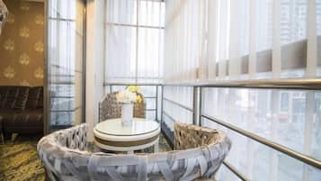 A corner room with a round table, wicker chairs, a sofa, and a view of the city through large windows.