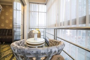 Une pièce d’angle avec une table ronde, des chaises en osier, un canapé et une vue sur la ville grâce à de grandes fenêtres.