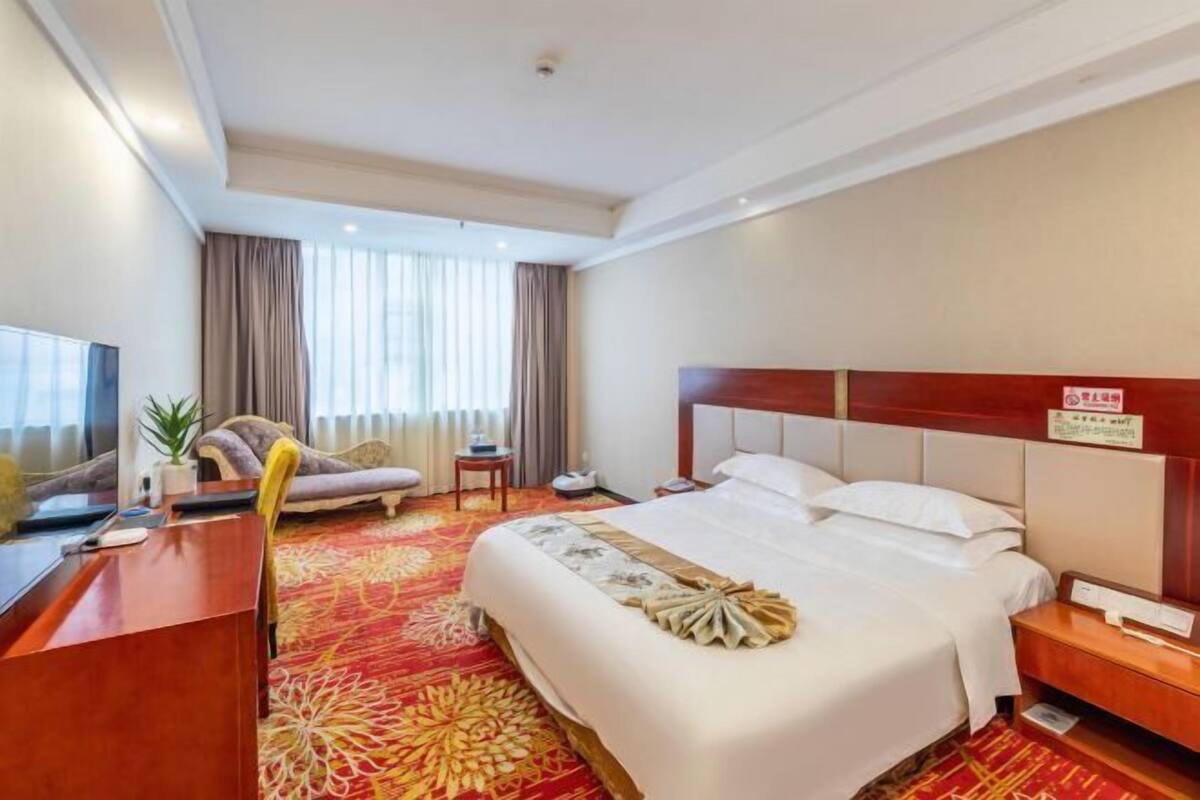 Ein Hotelzimmer mit Bett, Schreibtisch, Stuhl, Fernseher und einem Fenster mit Vorhängen.