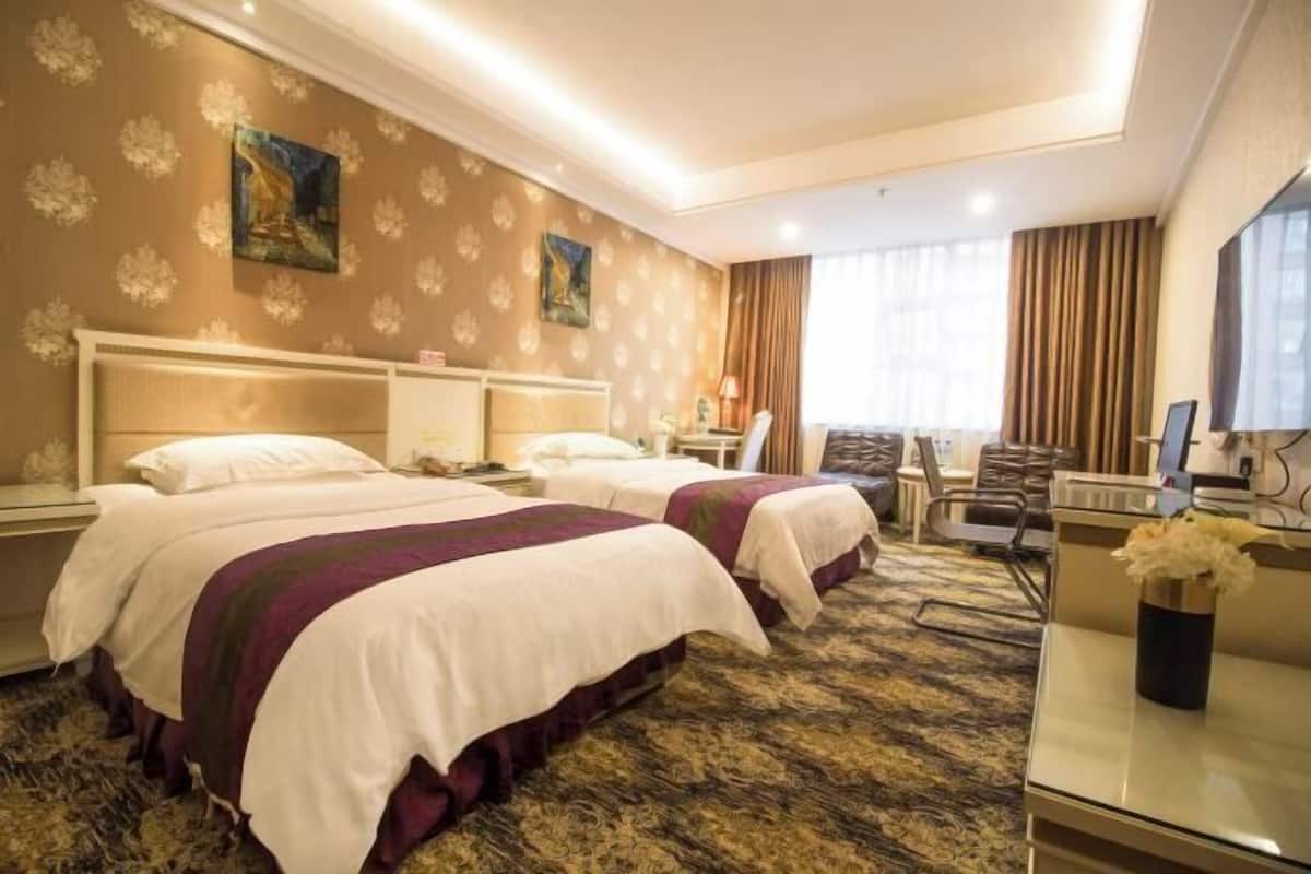 Ein Hotelzimmer mit zwei Betten, einem Schreibtisch, einem Stuhl, einem Fernseher und einem Fenster mit Vorhängen.