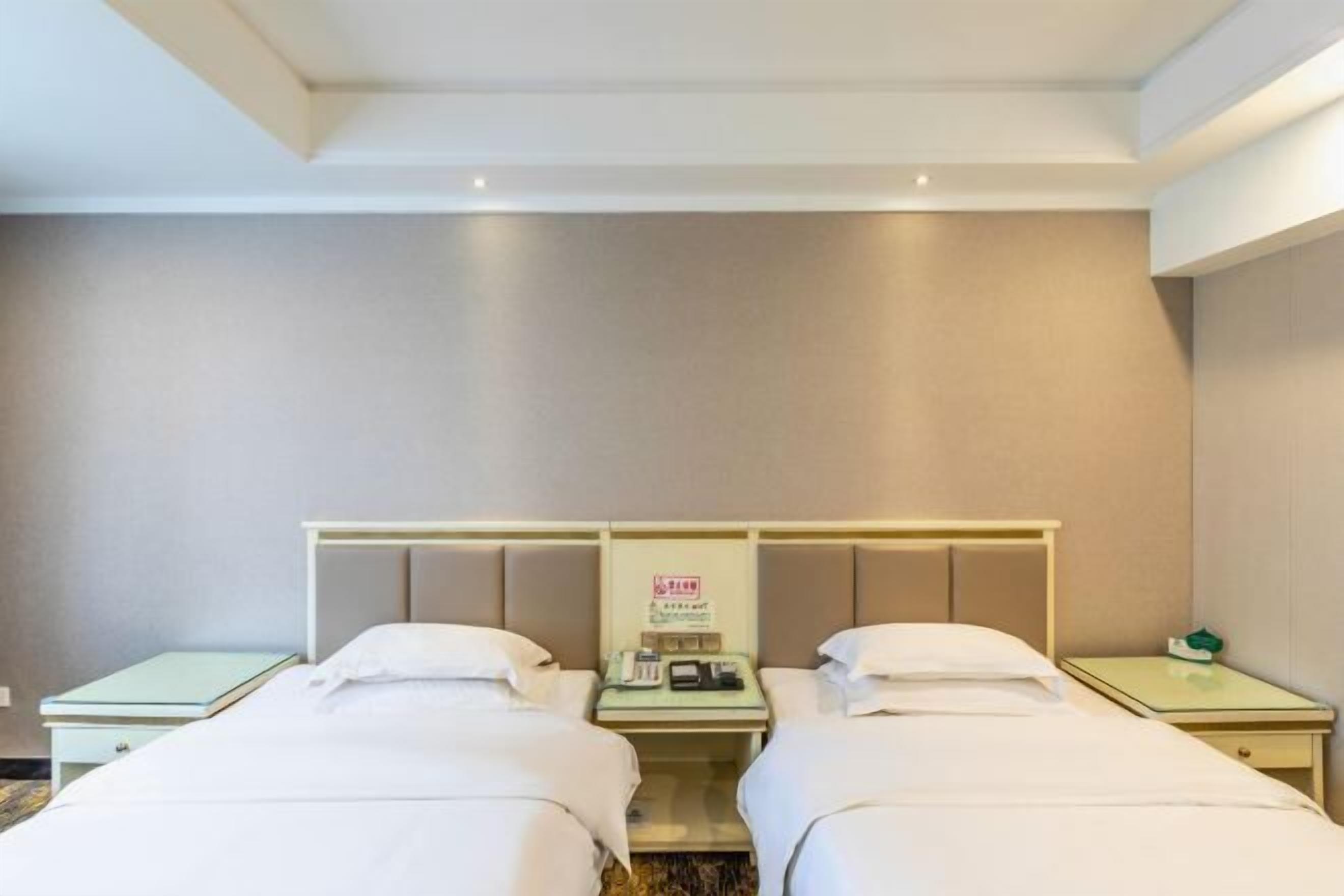 Una habitación de hotel con dos camas, una mesita de noche con un teléfono y una pequeña mesa con un objeto verde.