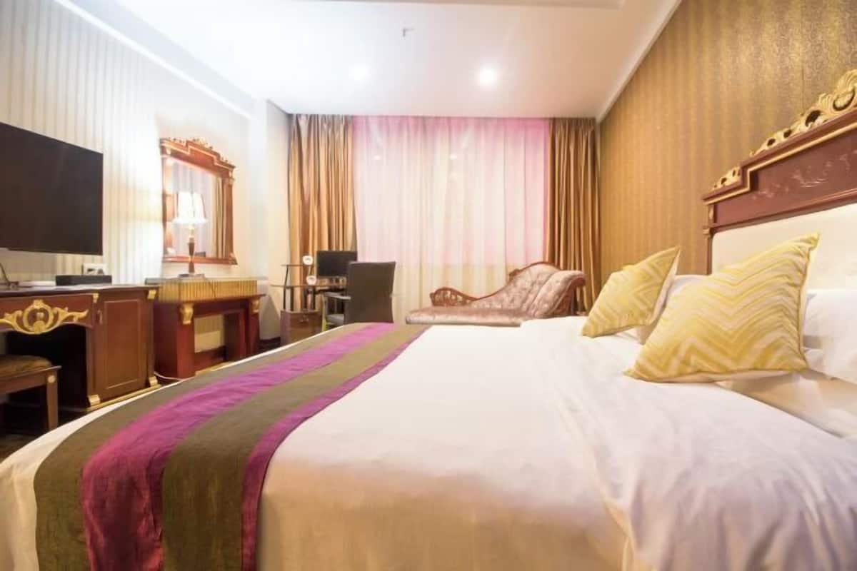 Ein Hotelzimmer mit einem großen Bett, einem Schreibtisch mit Computer, einem Sessel und einem Fernseher.