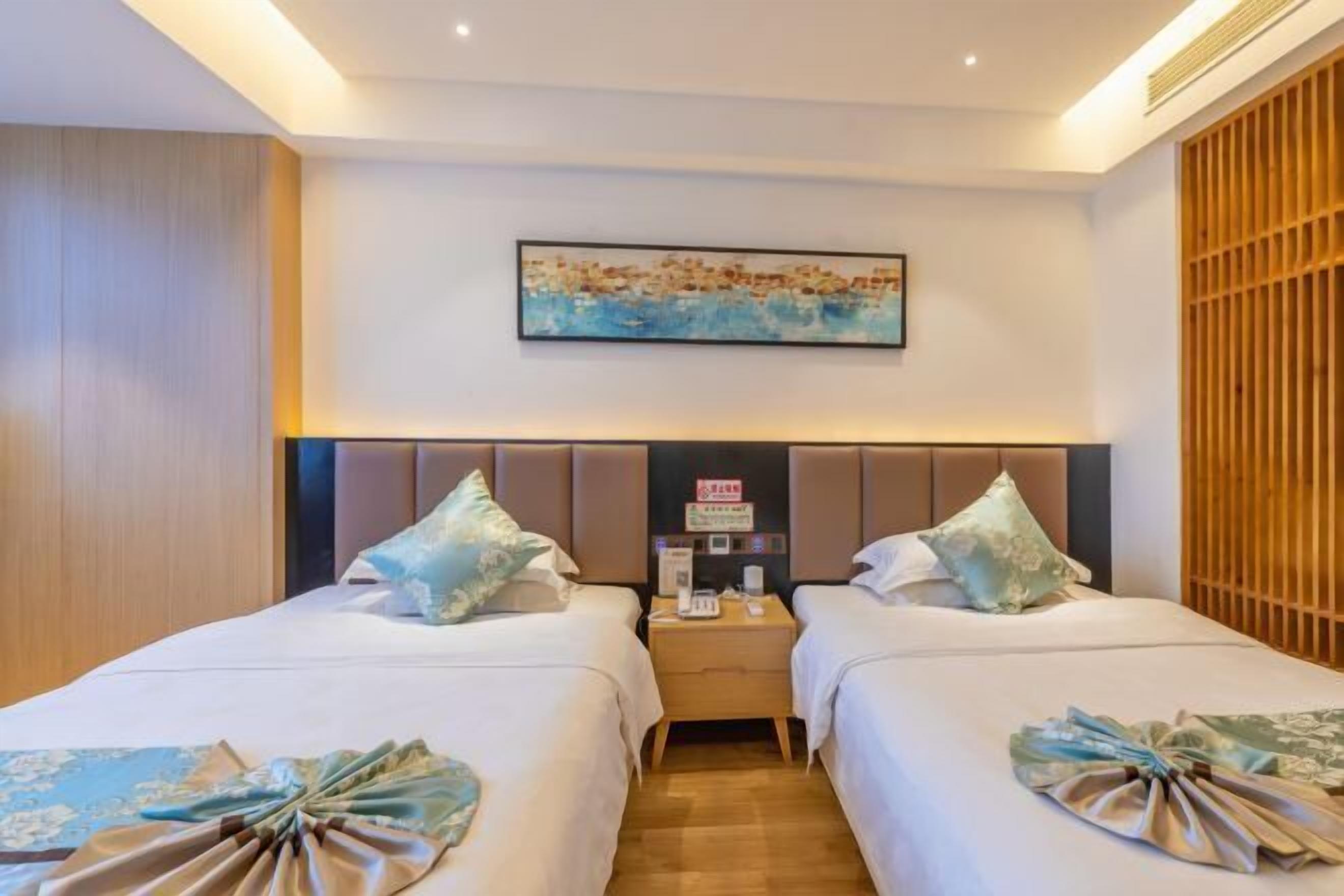 A hotel room with two beds, a headboard with a control panel, a wooden panel wall, and a painting above the beds.