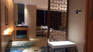 A hotel room with a bed, a small table, a decorative partition, and a view of the living area. - Mei YI Hotel (Yiliang)