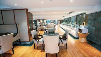 En moderne hotellobby med et langt spisebord, komfortable siddepladser og udsigt over byen gennem store vinduer.