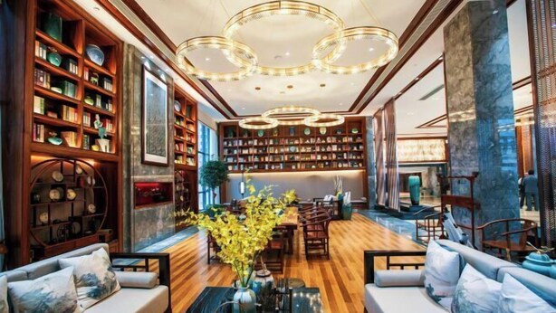 A spacious lobby with a wooden floor, a central seating area with sofas, a large bookshelf, and a decorative chandelier. - Mei YI Hotel (Yiliang)