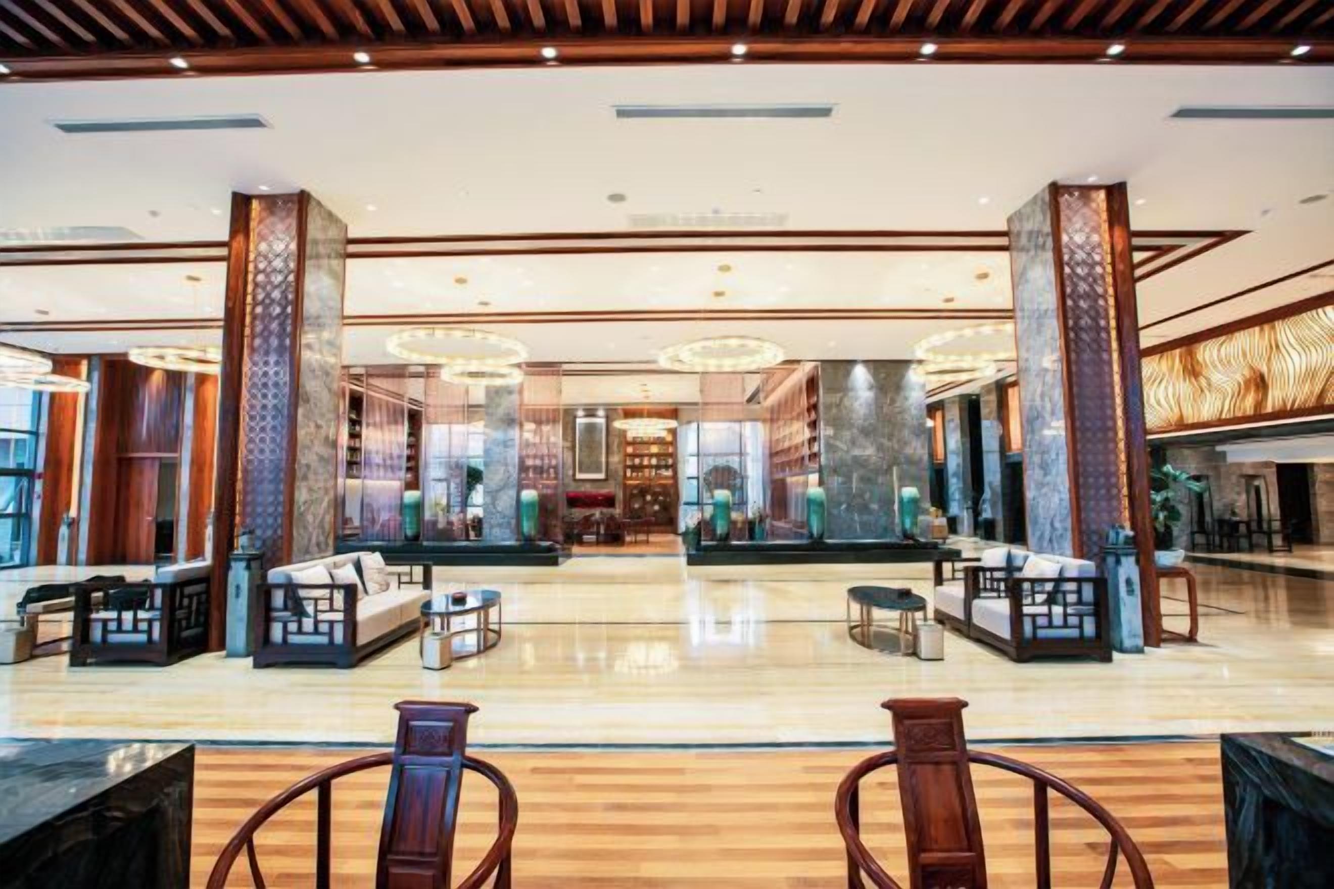 A spacious lobby with a central seating area, a reception desk, and a large mirror reflecting the space.