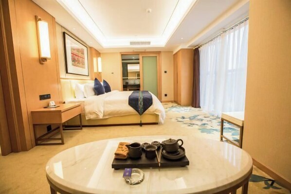 Habitación de hotel con cama, mesita de noche, una mesa redonda con juego de té, un armario y una ventana con cortinas.