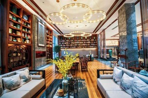 Uma biblioteca ampla com estantes, uma área central de estar e um lustre moderno.