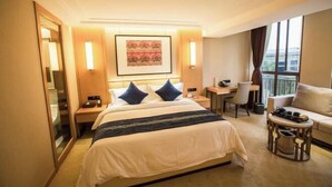 A hotel room with a bed, bedside tables, a desk, a chair, a sofa, and a large window.