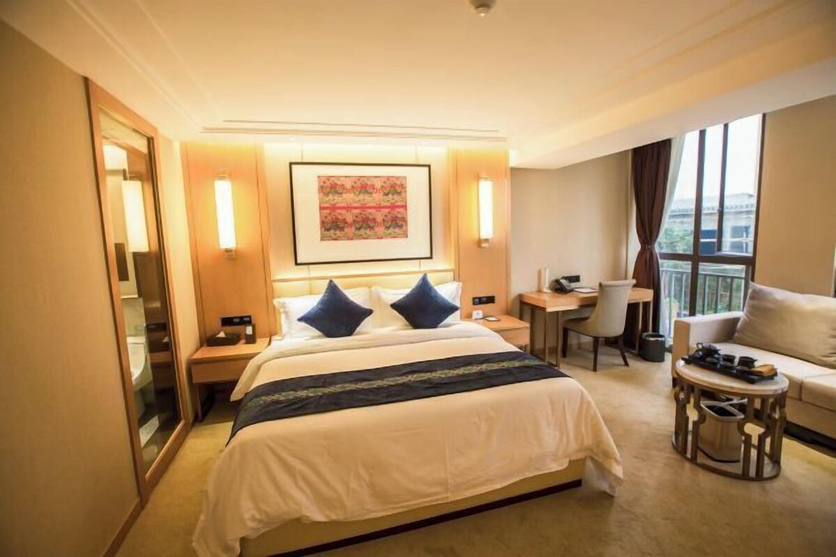 Habitación de hotel con cama, mesitas de noche, escritorio, silla, sofá y un ventanal grande.