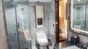 A modern bathroom with a glass-enclosed shower, a toilet, a large mirror, and a marble countertop.
