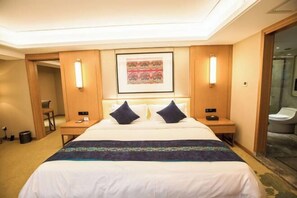 Habitación de hotel con una cama grande, dos mesitas de noche, un cuadro enmarcado sobre la cama y un box de ducha de vidrio.