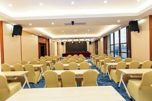 Un salón de conferencias con mesas y sillas dispuestas en filas, un escenario y una pantalla grande.