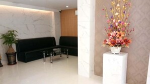 A modern lobby with a black sofa, a white vase with flowers, and a marble wall. - Jielv Hotel (Puning)