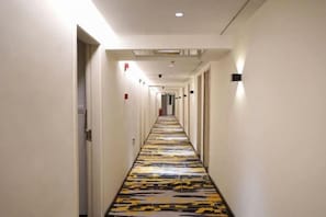 A long, narrow hotel corridor with a patterned floor, doors on both sides, and a ceiling with recessed lighting.