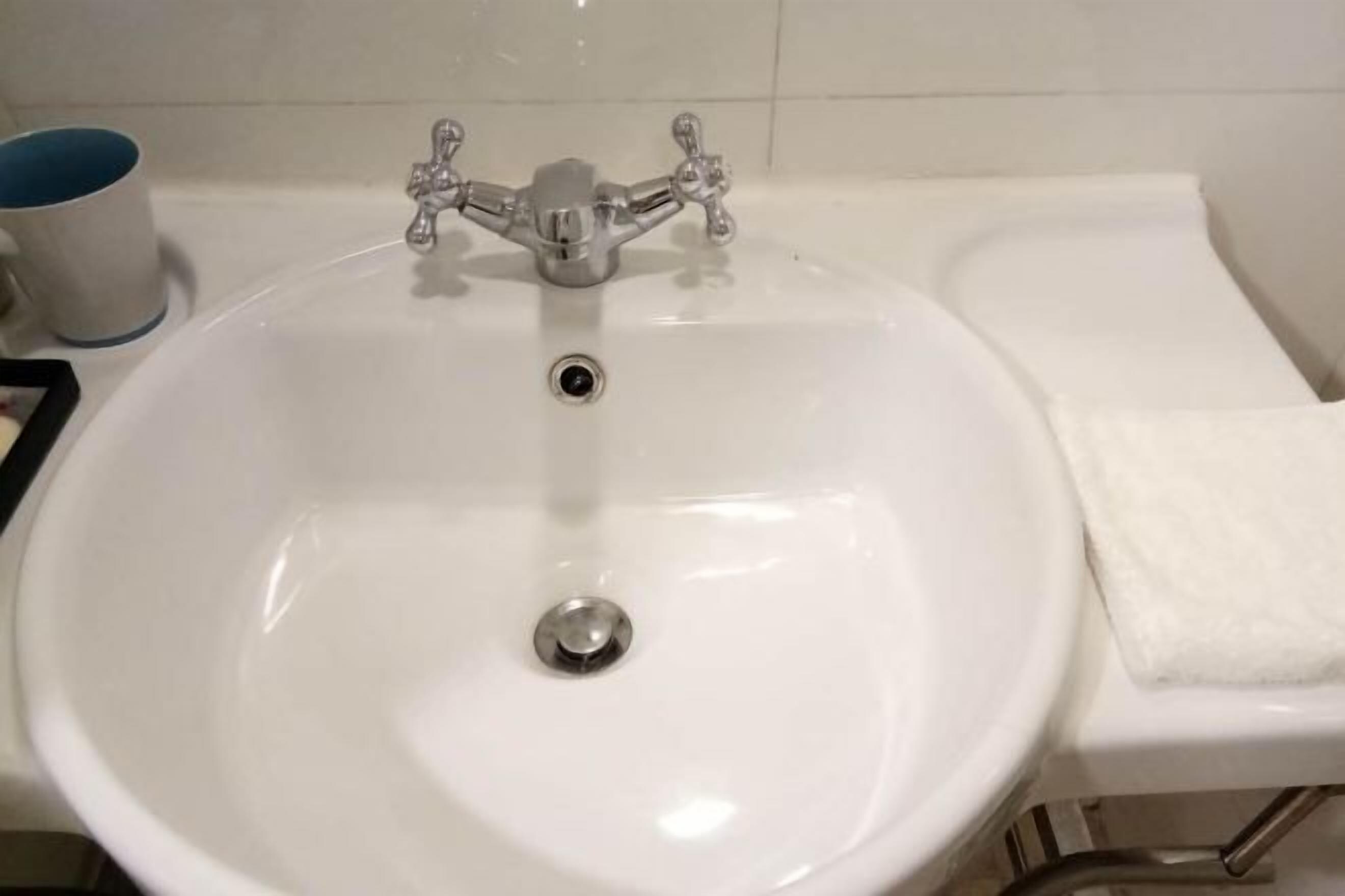 Un lavabo blanc dans une salle de bain, avec un robinet chromé et une serviette posée sur le côté droit.