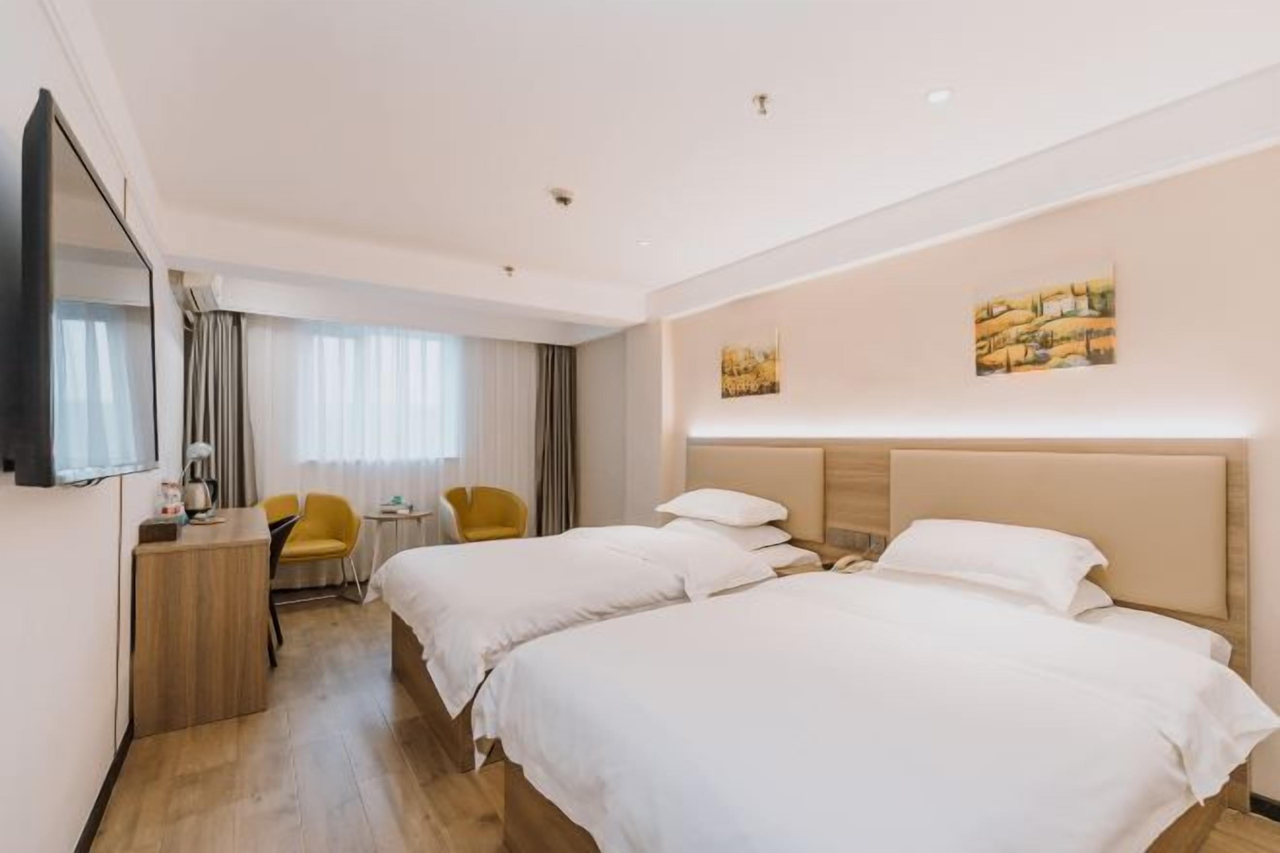 A hotel room with two beds, a desk, a chair, and artwork on the walls.