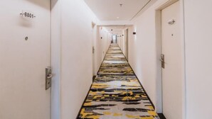 A hotel hallway with a patterned floor, doors on either side, and a number sign on the left wall. - Jielv Hotel (Puning)
