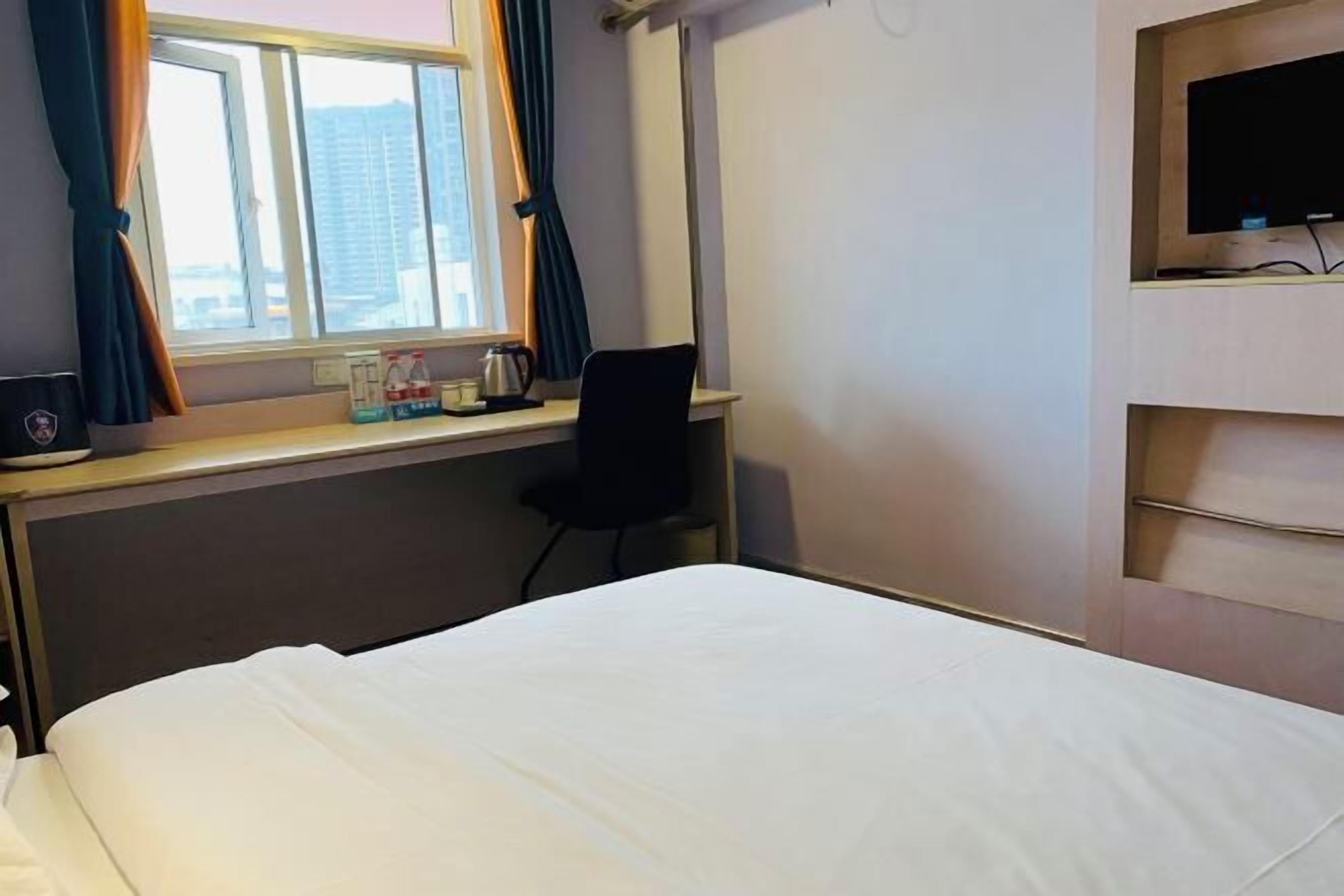 A hotel room with a bed, a desk with a chair, a TV, and a window with curtains.
