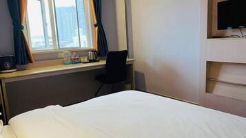 A hotel room with a bed, a desk with a chair, a TV, and a window with curtains.