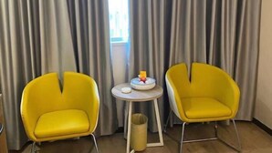 A room with two yellow chairs, a small round table with a white base, and a trash bin. - Jielv Hotel (Puning)