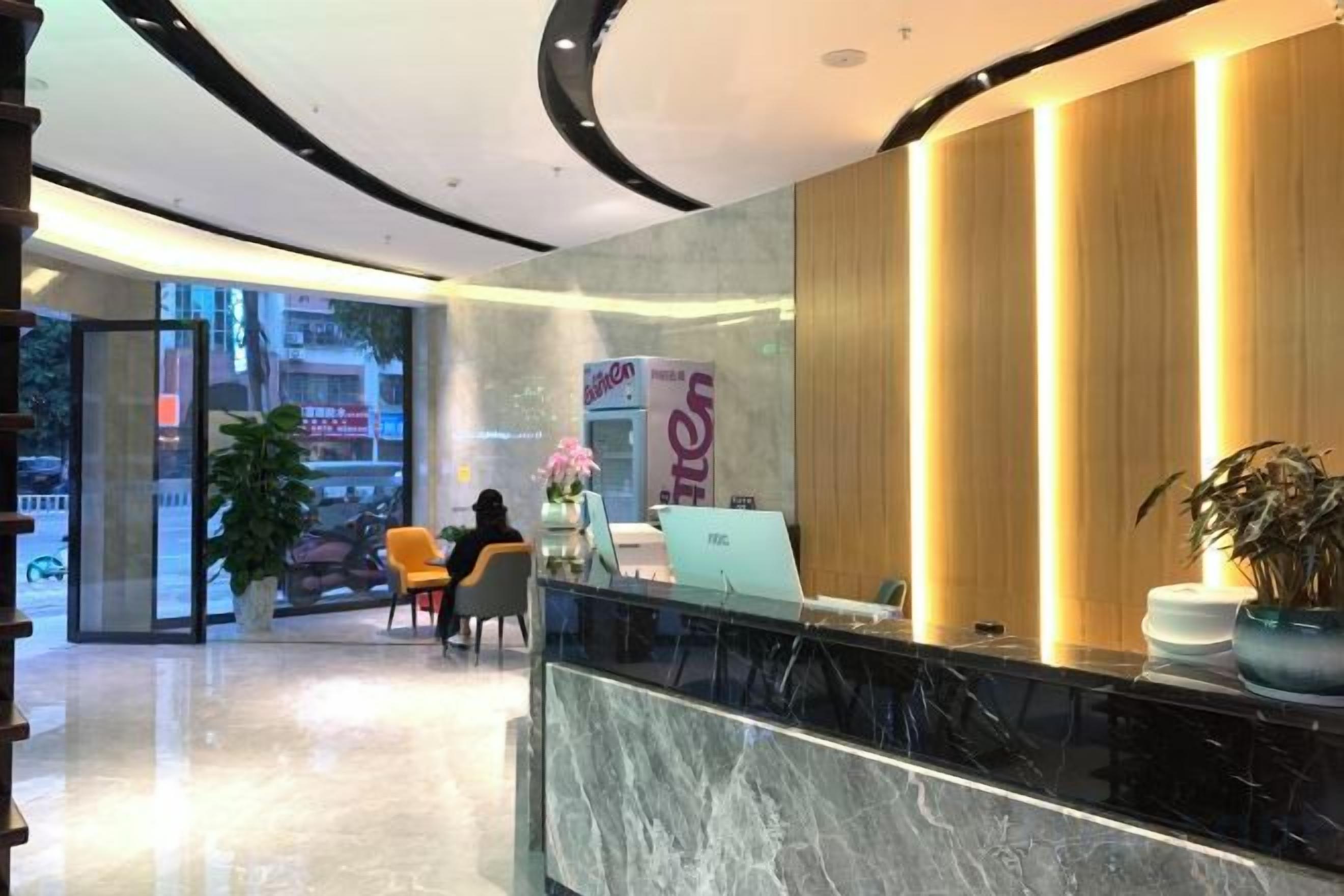 Un espace d’accueil d’hôtel avec un comptoir en marbre, un bureau d’accueil et une grande plante en pot.