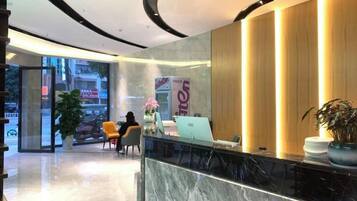 Un espace d’accueil d’hôtel avec un comptoir en marbre, un bureau d’accueil et une grande plante en pot.