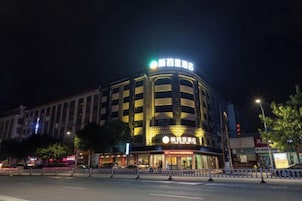 Un hotel de varios pisos con un letrero llamativo en la parte superior, una amplia entrada con marquesina y una fachada bien iluminada.
