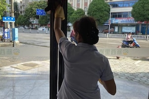 A person standing by a window, holding a piece of clothing.