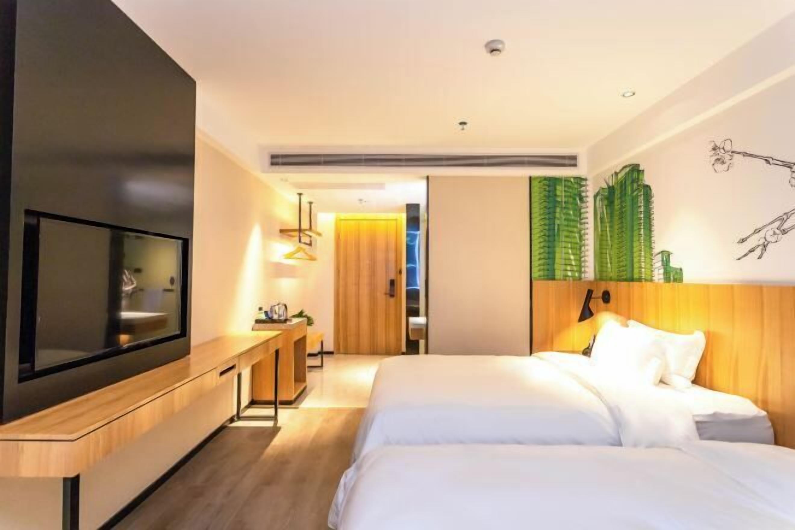 Una habitación de hotel moderna con un televisor de pantalla plana grande, un escritorio de madera, una cama con ropa blanca y un mural verde en la pared.