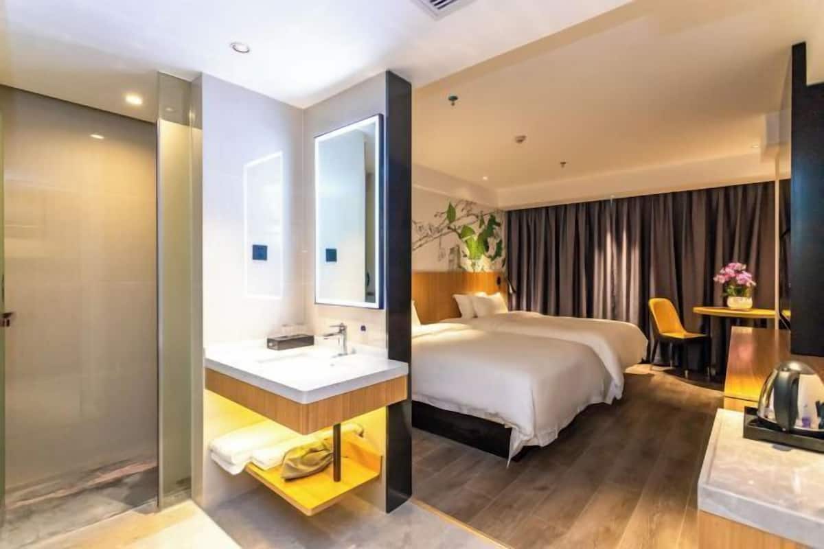 A hotel room with a large bed, a separate sitting area with a chair, a desk, and a small table with a lamp.
