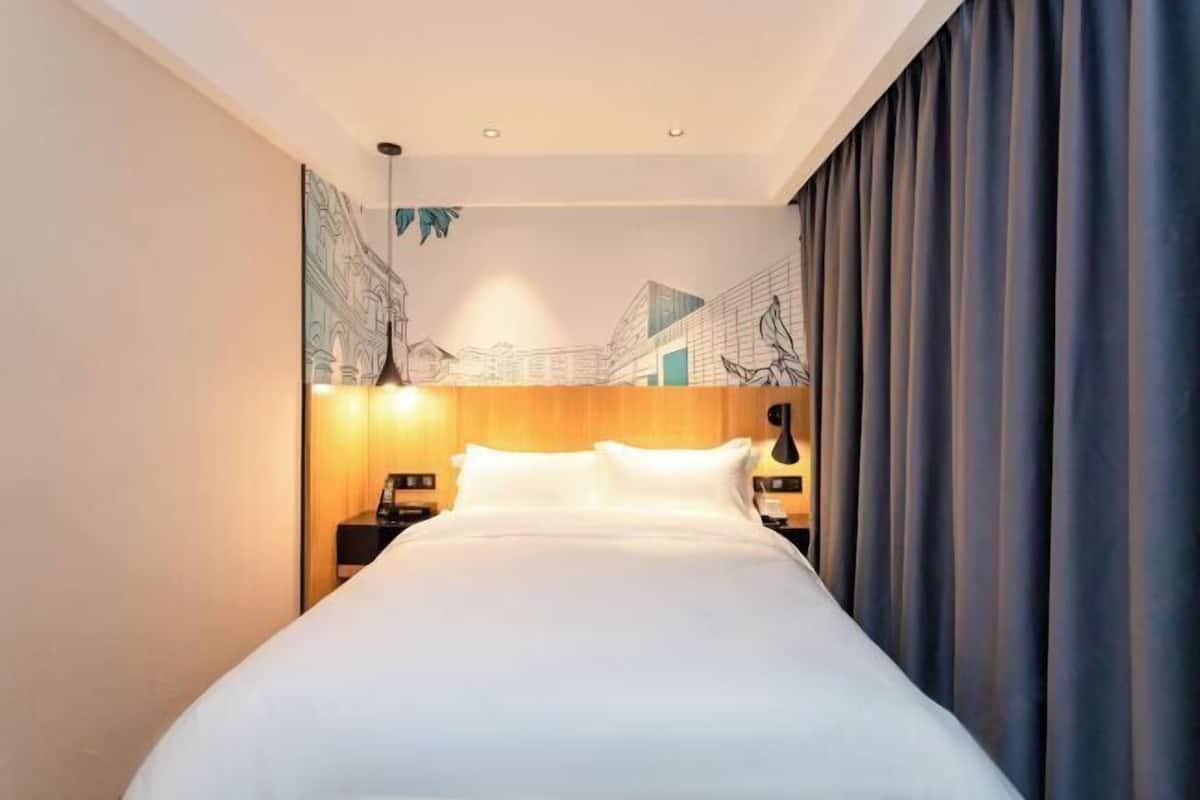 A hotel room with a large bed, a wooden headboard, a nightstand with a lamp, and a wall mural.
